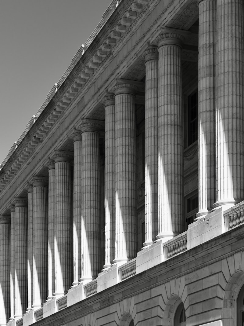 Columnata de un edificio judicial neoclásico, con sombras marcadas por el sol.