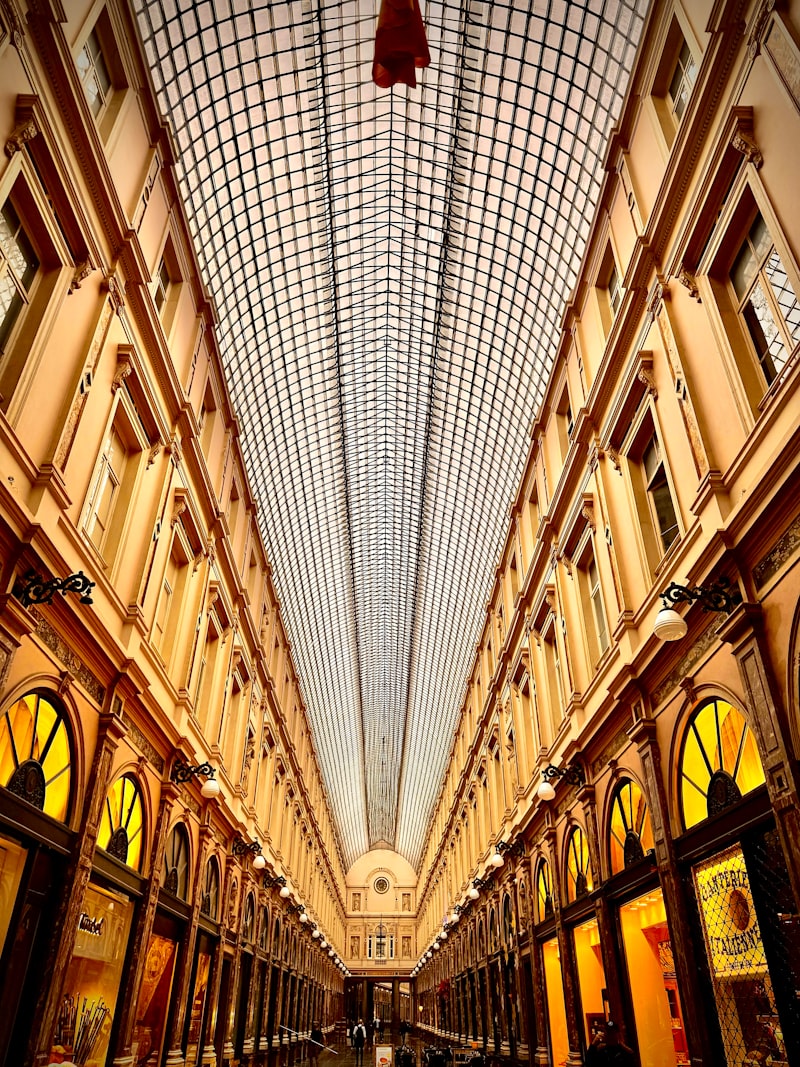 Interior de una galería comercial monumental con techo vidriado, en perspectiva simétrica.